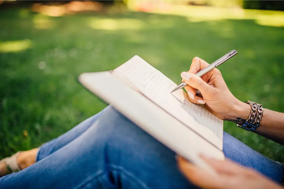 woman sitting on the grass writing in a journal